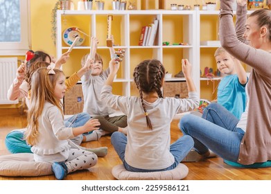 Kindergarten teacher with children sitting on the floor having music class, using various instruments and percussion. Early music education - Shutterstock ID 2259586121