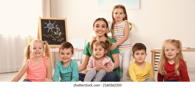 Kindergarten Teacher With Group Of Children In Playroom. Banner Design