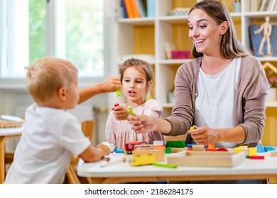 Kindergarten Teacher Playing Together With Children At Colorful Preschool Classroom. Mother Playing With Children.