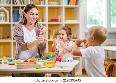 Kindergarten Teacher Playing Together With Children In The Colorful Preschool Classroom. Mother Playing With Children.
