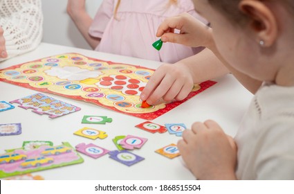 A kindergarten teacher plays a board game with two little girls. Mom plays with little daughters - Shutterstock ID 1868515504