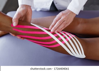 Kinesiology taping. Physiotherapist applying kinesiology tape to patient calf muscle.Therapist treating young female African American athlete. Post traumatic rehabilitation, sport physical therapy.
