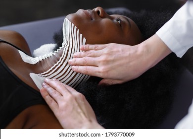 Kinesiology taping. Physiotherapist applying kinesiology tape to patient neck. Therapist treating young female African American athlete. Post traumatic rehabilitation, sport physical therapy. - Powered by Shutterstock