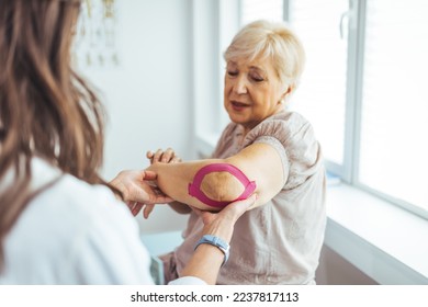 Kinesiology taping treatment with pink tape on senior patient injured arm. Woman hands apply kinesio treatment after muscle injury. A Modern rehabilitation physiotherapy worker with woman client - Powered by Shutterstock