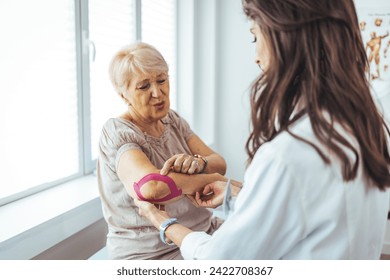 Kinesiology taping treatment with pink tape on senior patient injured arm. Woman hands apply kinesio treatment after muscle injury. A Modern rehabilitation physiotherapy worker with woman client - Powered by Shutterstock