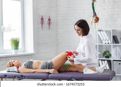 Kinesiology Taping.Physical Therapist Applying Kinesiology Tape To Patient Knee.Therapist Treating Injured Knee Of Young Athlete.Post Traumatic Rehabilitation, Sport Physical Therapy,recovery Concept.