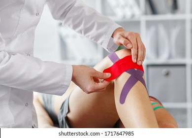 Kinesiology Taping.Physical Therapist Applying Kinesiology Tape To Patient Knee.Therapist Treating Injured Knee Of Young Athlete.Post Traumatic Rehabilitation, Sport Physical Therapy,recovery Concept.