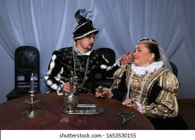 King Henry And Queen Marguerite Of Navarre Drink Sitting At The Table. Historical Reconstruction Of Medieval Costumes. Family Scene Of The French Royal Couple In 16th Century.