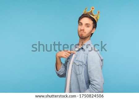 I'm king! Portrait of ambitious man wearing golden crown and pointing himself, looking with arrogance, declaring his authority, superior privileged status. studio shot isolated on blue background