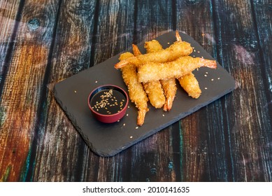 King prawns battered in panko raincoat with a bowl of soy sauce and sesame seeds on a black slate plate