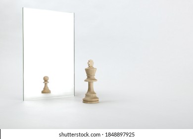 the king is reflected in the mirror as a pawn on white background. underestimation of their abilities - Shutterstock ID 1848897925