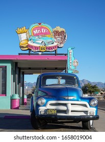 Kingman, Arizona / USA - 21 Oct 2019: A Blue Vintage Chevrolet 3100 Farm Truck Sits Outside A Colourful Route 66 Diner With Pink / Green Paint, Neon Burger And Root Beer Sign Against A Clear Blue Sky.