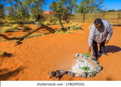 Kings Creek, Australia - Aug 21, 2019: Aboriginal Burns Plants On Fire Surrounded By Stones. Plants Have Special Purifying Properties In The Smoking Ceremony Of The Australian Natives.