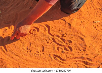 Kings Creek Station, Northern Territory, Australia - Aug 21, 2019: aboriginal woman hands creating shapes with red sand on the ground in aboriginal art style.