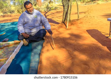 Kings Creek Station, Northern Territory, Australia - Aug 21, 2019: aboriginal guide man creating shapes with red sand on the ground in aboriginal art style. Karrke Aboriginal Cultural Experience tour.