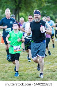 Kings Park, New York, USA - 17 June 2019: A Father And Son Give The Thumbs Up Sign While Running A 10K Trail Race During The NY State Parks Sunken Meadow Summer Series Race.