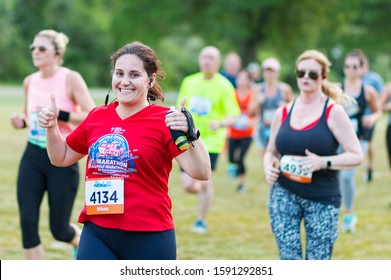 Kings Park, New York, USA - 17 June 2019: A Runner Racing A 10K Is Smiling And Giving Two Thumbs Up While Carrying Her Water Bottle Suring The Sunken Meadow State Park Summer Series Race.