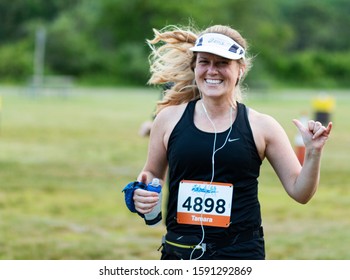 Kings Park, New York, USA - 17 June 2019: Runner Racing A 10K Is Smiling And Giving Hang Loose Sign While Carrying Water Bottle In The Other Hand During The Sunken Meadow State Park Summer Series