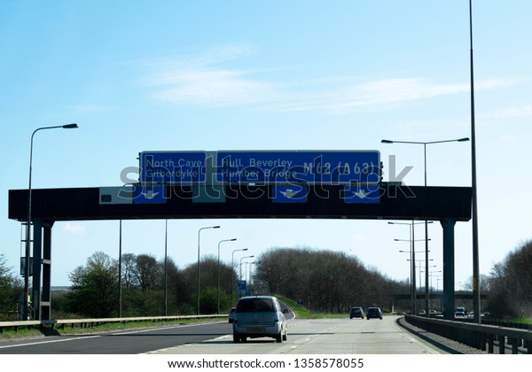 Kingston upon Hull,\
Britain - March 31st 2019: Road sign above motorway to Kingston\
upon Hull, Beverley, Humber Bridge in Britain UK with driving cars\
on a clear blue sky 