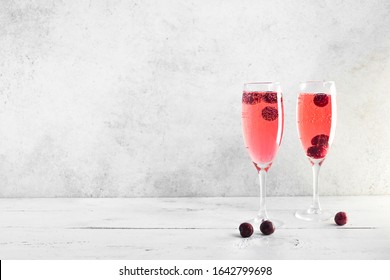 Kir Royal Champagne Cocktail on white, copy space. Flute glasses with berry sparkling champagne drink for celebrating or chilling.