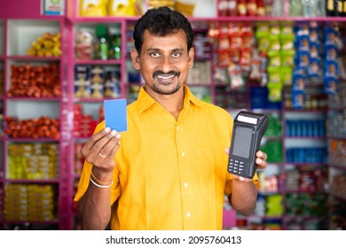 Kirana Or Groceries Merchant Showing Credit Card And Swiping POS Machine - Concept Of Accepting Digital Payment In Retail Business, Cashless Purchase And E-payment