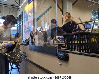 Kirkland, WA / USA - Circa April 2020: Cashier Behind A Plexiglass Wall At A Checkout Counter Inside A QFC Grocery Store During The Coronavirus Outbreak