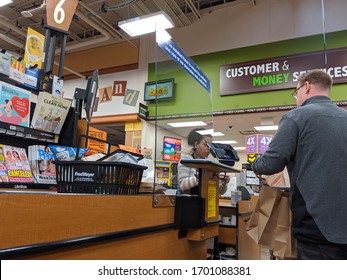 Kirkland, WA / USA - Circa April 2020: Cashier Behind A Plexiglass Wall At A Checkout Counter Inside A Fred Meyer Grocery Store During The Coronavirus Outbreak