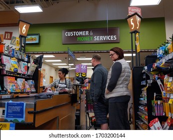 Kirkland, WA / USA - Circa April 2020: Cashier Behind A Plexiglass Wall At A Checkout Counter Inside A Fred Meyer Grocery Store During The Coronavirus Outbreak