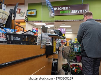 Kirkland, WA / USA - Circa April 2020: Cashier Behind A Plexiglass Wall At A Checkout Counter Inside A Fred Meyer Grocery Store During The Coronavirus Outbreak