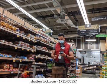 Kirkland, WA / USA - Circa April 2020: Grocery Store Worker Scanning Bready Inventory And Restocking Shelves, While Wearing A Face Mask During The COVID-19 Pandemic.