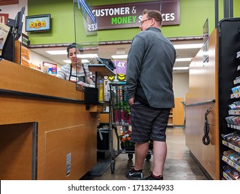 Kirkland, WA / USA - Circa April 2020: Cashier Behind A Plexiglass Wall At A Checkout Counter Inside A Fred Meyer Grocery Store During The Coronavirus Outbreak