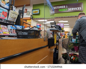 Kirkland, WA / USA - Circa April 2020: Cashier Behind A Plexiglass Wall At A Checkout Counter Inside A Fred Meyer Grocery Store During The Coronavirus Outbreak