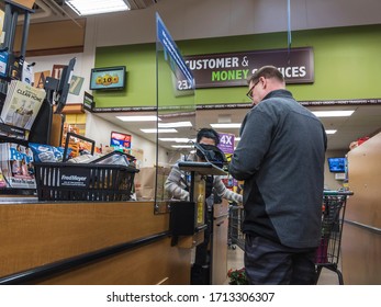 Kirkland, WA / USA - Circa April 2020: Cashier Behind A Plexiglass Wall At A Checkout Counter Inside A Fred Meyer Grocery Store During The Coronavirus Outbreak