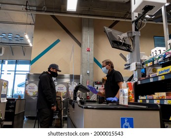 Kirkland, WA USA - Circa April 2020: Cashier Behind A Plexiglass Wall At A Checkout Counter Inside A QFC Grocery Store During The Coronavirus Outbreak