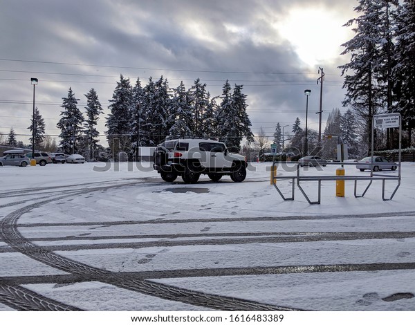 Kirkland, WA / USA - circa January 2020: tire\
tracks in the ice and snow in a parking lot with snowy covered cars\
after a big storm.