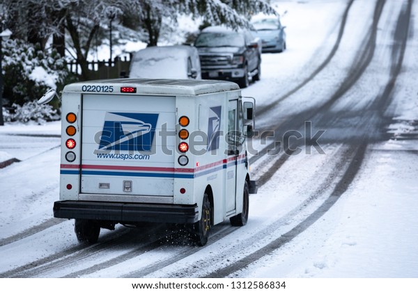 Kirkland, Washington / USA - February 8 2019:  \
United States Postal Service (USPS) delivery truck driving down a\
snowy residential street during a winter storm, with space for text\
on the right
