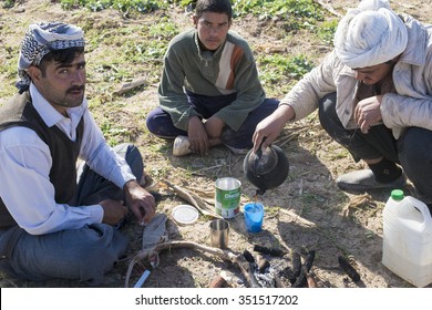 Kirkuk, Iraq - December 4, 2015: Bunch Of Arab Farmers Or Shepherds Drink Tea While Sitting In Dry Ground In Iraqi Desert 