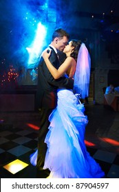 Kiss and dance young bride and groom in dark banqueting hall