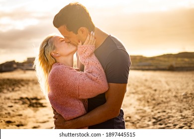 Kiss and love couple outdoor with two young man and woman kissing and hugging in a golden sunset background - people enjoy together forever life - concept of different ages male female
