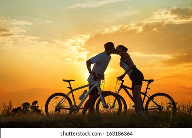 Kiss of romantic young couple on bicycles against sunset - Powered by Shutterstock