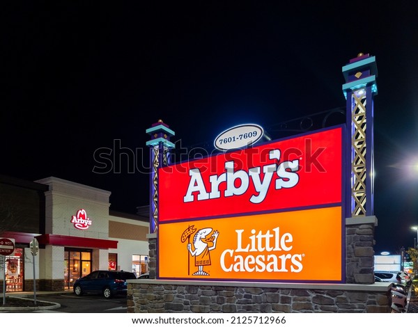 Kissimmee, Florida - February 4, 2022: Closeup\
Night View of Arby\'s and Little Caesars Billboard in Foreground and\
Arby\'s Building in\
Background