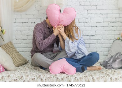 kissing guy and girl who are closing with a pink heart, sitting on the bed against a white brick wall
 - Powered by Shutterstock