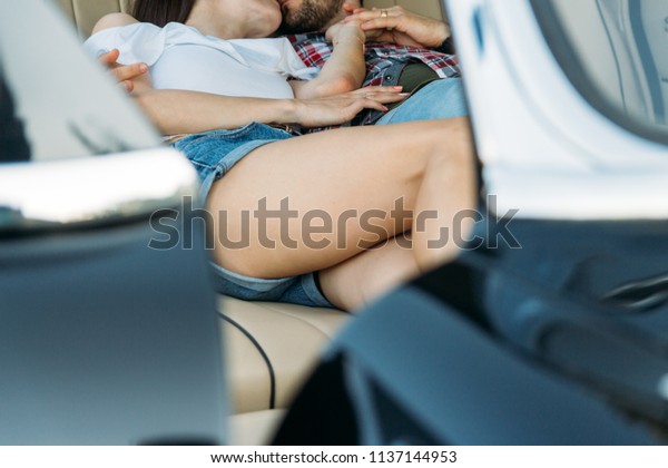 kissing people who are lying in the car and holding\
hands. dressed in a plaid shirt, shorts and jeans, a white blouse.\
on his hand a watch and a gold chain, a ring. pry. look through the\
window in the