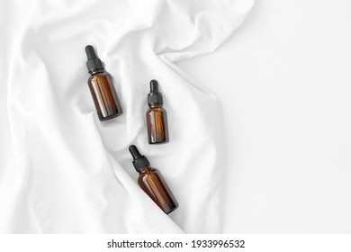 Kit of brown dropper glass bottles with pipette on white fabric background. Zero waste glass containers. Serum, oil, acid, lotion. Organic, natural cosmetic. Beauty, skincare. Spa products
