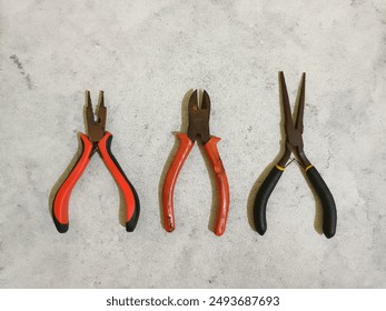 Kit pliers tools with black and red rubber handles on white background. Snap ring, cutting pliers, nose pliers on the table. Pliers set on white concrete background. Working tools. Horizontal.