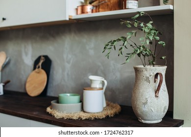 Kitchen appliances on a wooden table top, against a gray textured wall. Dry spikelets.vase in the foreground
