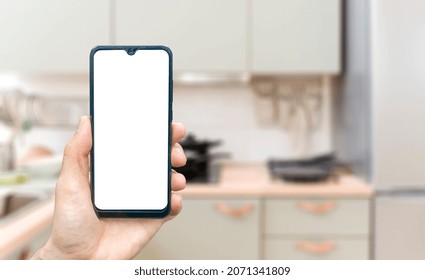 Kitchen background with hand with phone. Blurred home kitchen with blank smartphone screen. Online grocery ordering concept, online food shopping. - Powered by Shutterstock