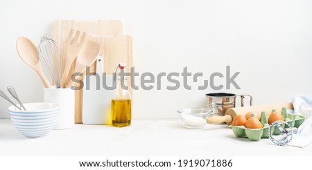 Kitchen background mockup with eggs, rolling pin, bowls for cooking and baking utensils on the table on white background. Blank space for a text, home kitchen decor concept. Wide banner.