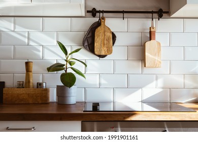 Kitchen Brass Utensils, Chef Accessories. Hanging Kitchen With White Tiles Wall And Wood Tabletop.Green Plant On Kitchen Background Early Morning Light Side View