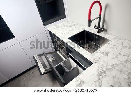Kitchen with built-in opened dishwasher and pull out drawer for waste bin separate waste collection. Water faucet sink built in compact high pressure laminate HPL countertop undermount installation.